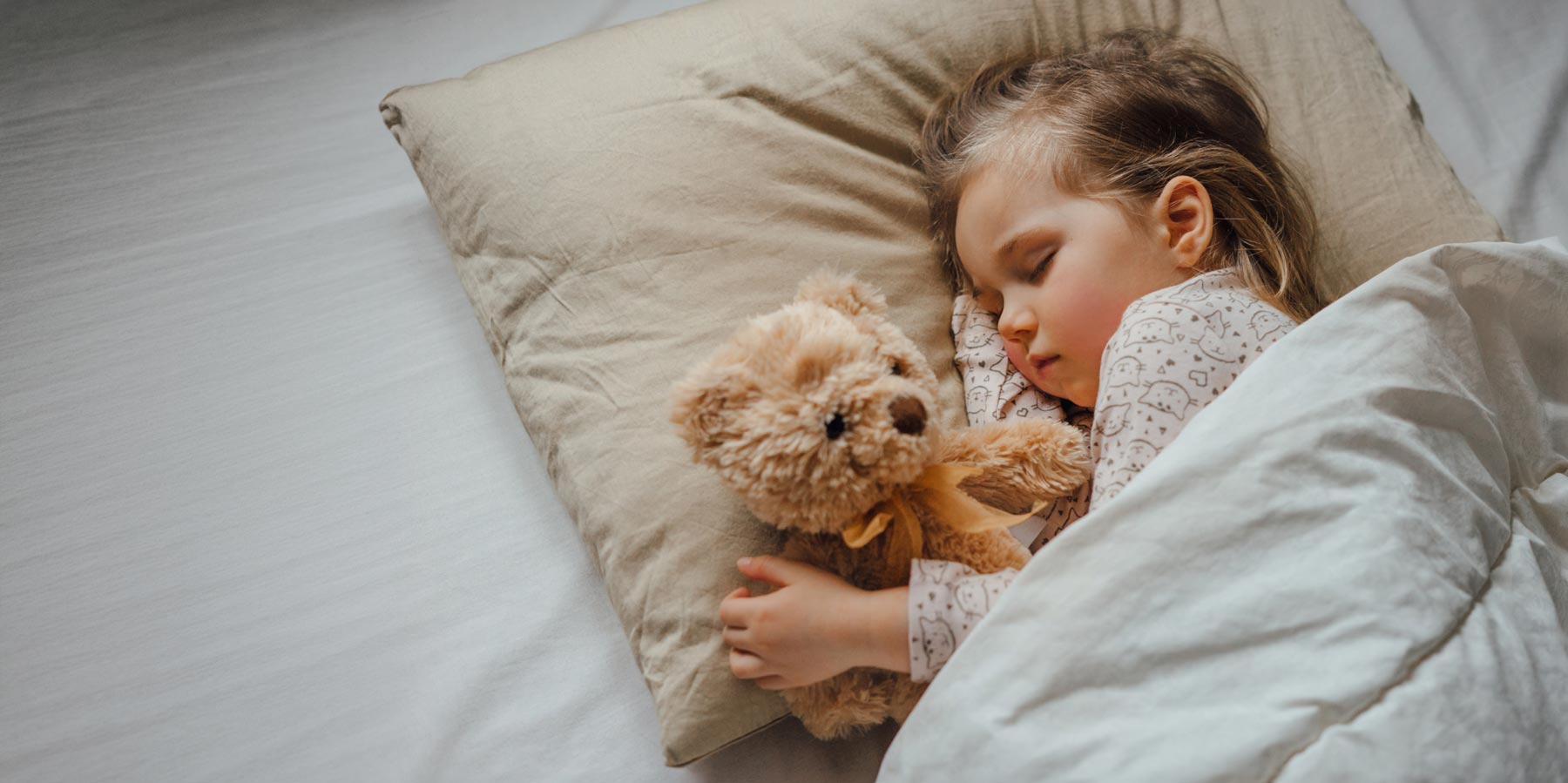 Child hugs teddy bear at bed.